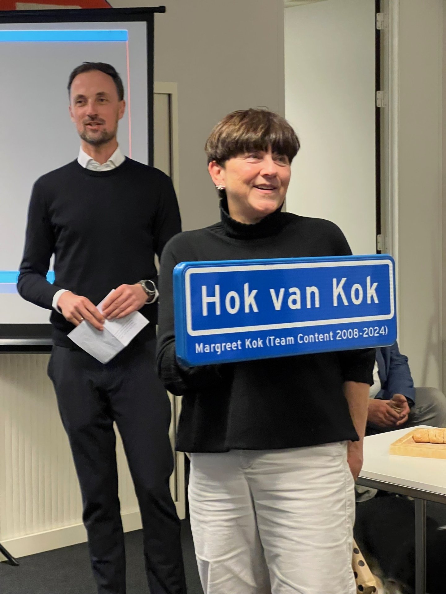Margreet bij haar afscheid met het verkeersbord 'Hok van Kok' wat nu in haar voormalige kantoor hangt.